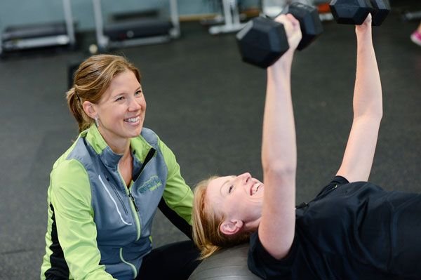 A trainer guiding a client through a core exercise with a dumbbell