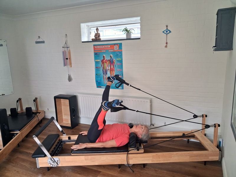 A client lying on the reformer working one leg at a time in the straps