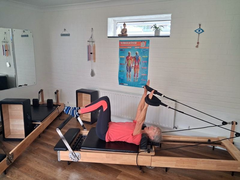 A client lying on the reformer with her feet in the straps and arms raised
